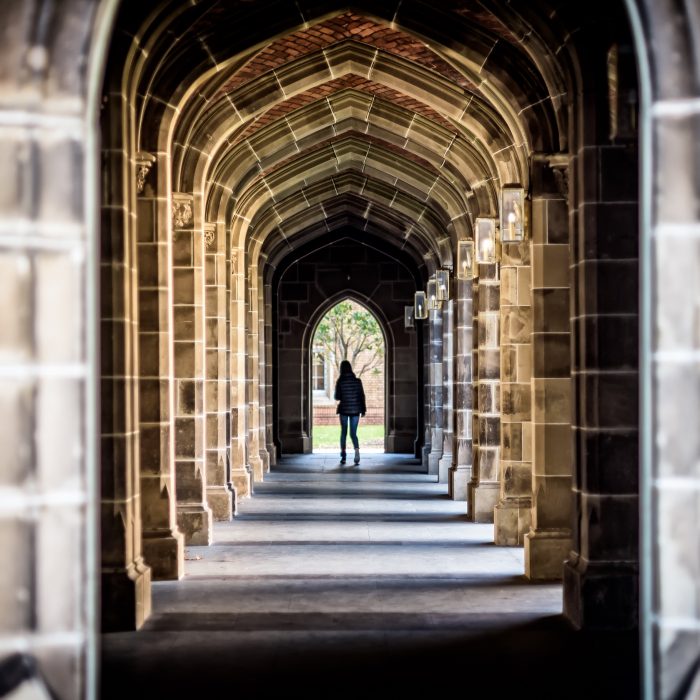 Woman standing at the end of a college campus stone archway path